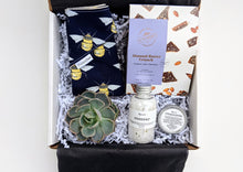 Load image into Gallery viewer, A sweet little token gift for new parents. This gift box includes Chocolate Almond Buttercrunch, Relaxing Bath Salts, Baby Bum Balm, an air plant or succulent and a beautiful hand made Baby Bib.  Our gifts come beautifully wrapped with a bow along with an art card including your personalized note.